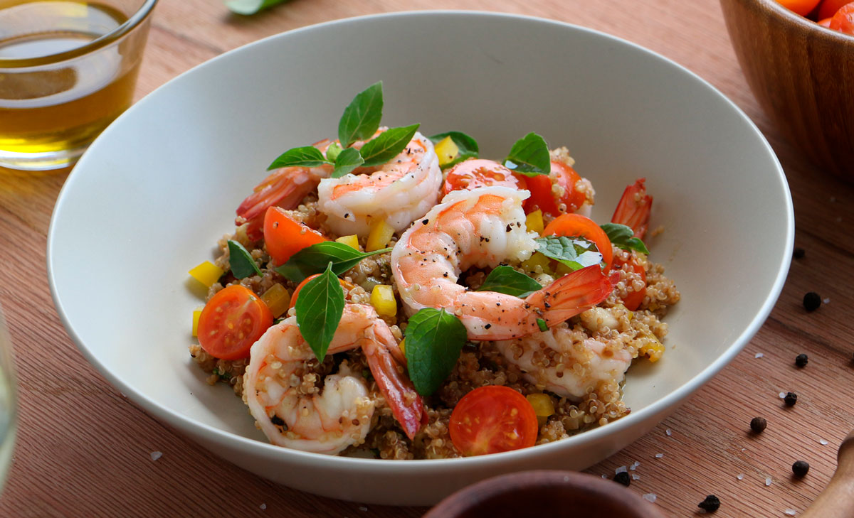 A white bowl filled with quinoa, shrimp, basil, mint, cherry tomatoes, and yellow peppers.