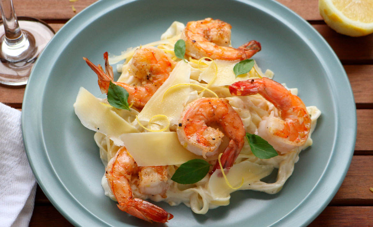 A plate of tagliatelle, shrimp, lemon sauce, topped with parmesan cheese and green spinach leaves.