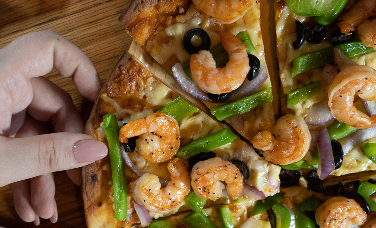 woman grabbing a slice of a shrimp pizza with del pacifico's wild blue mexican shrimp